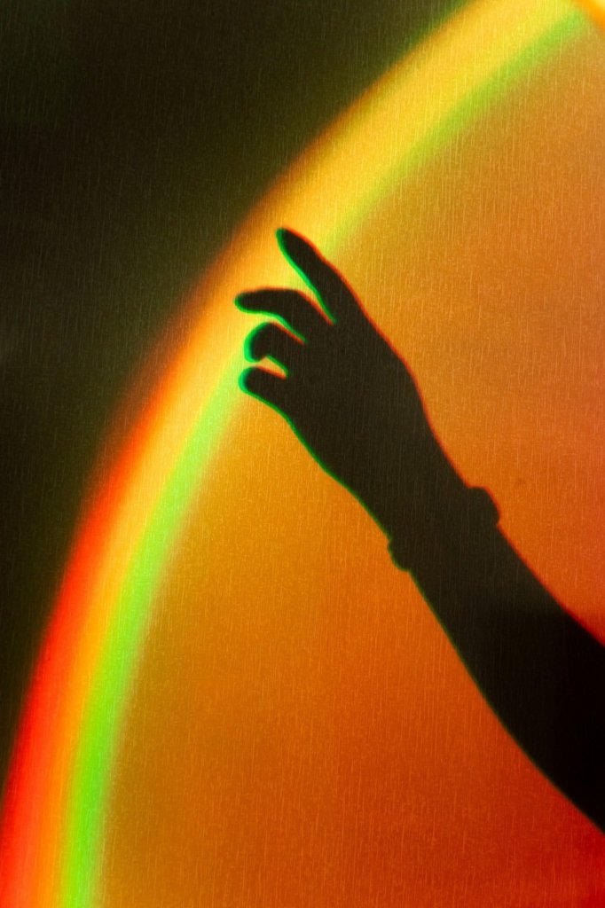 Ombre d'une main tendue vers un arc de lumière orange et vert